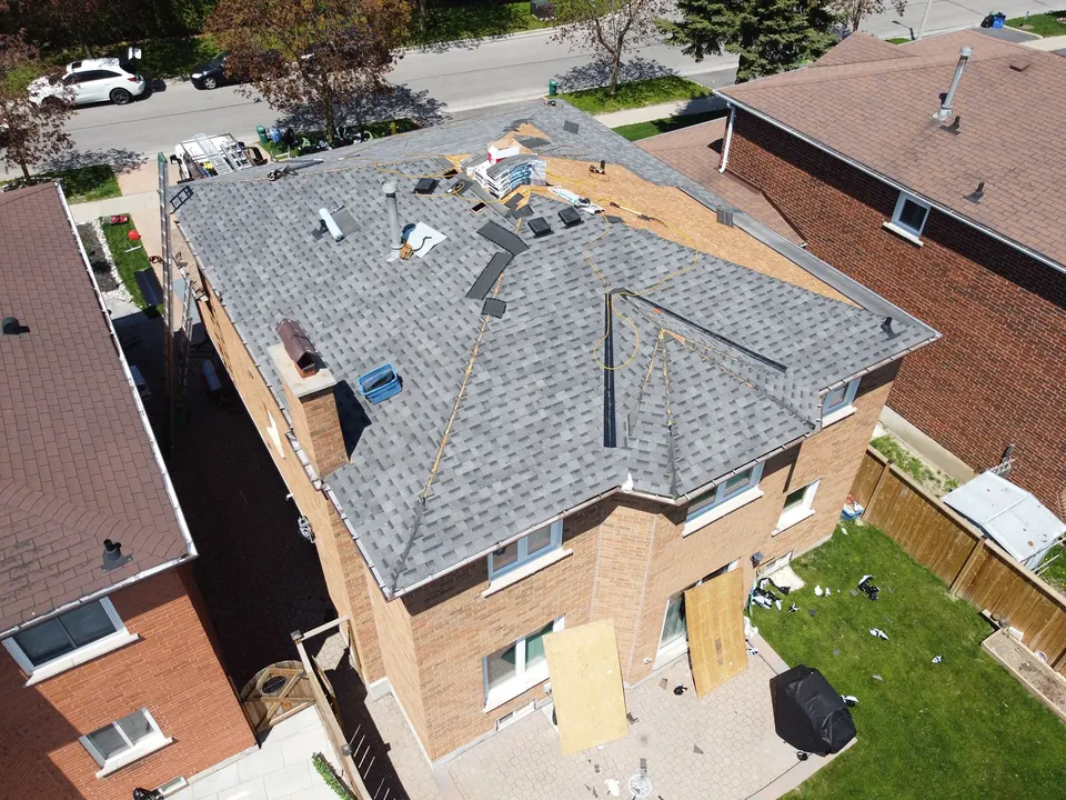 Drone view of a two-storey brick house partway through a re-roof, new grey shingles on most of the roof