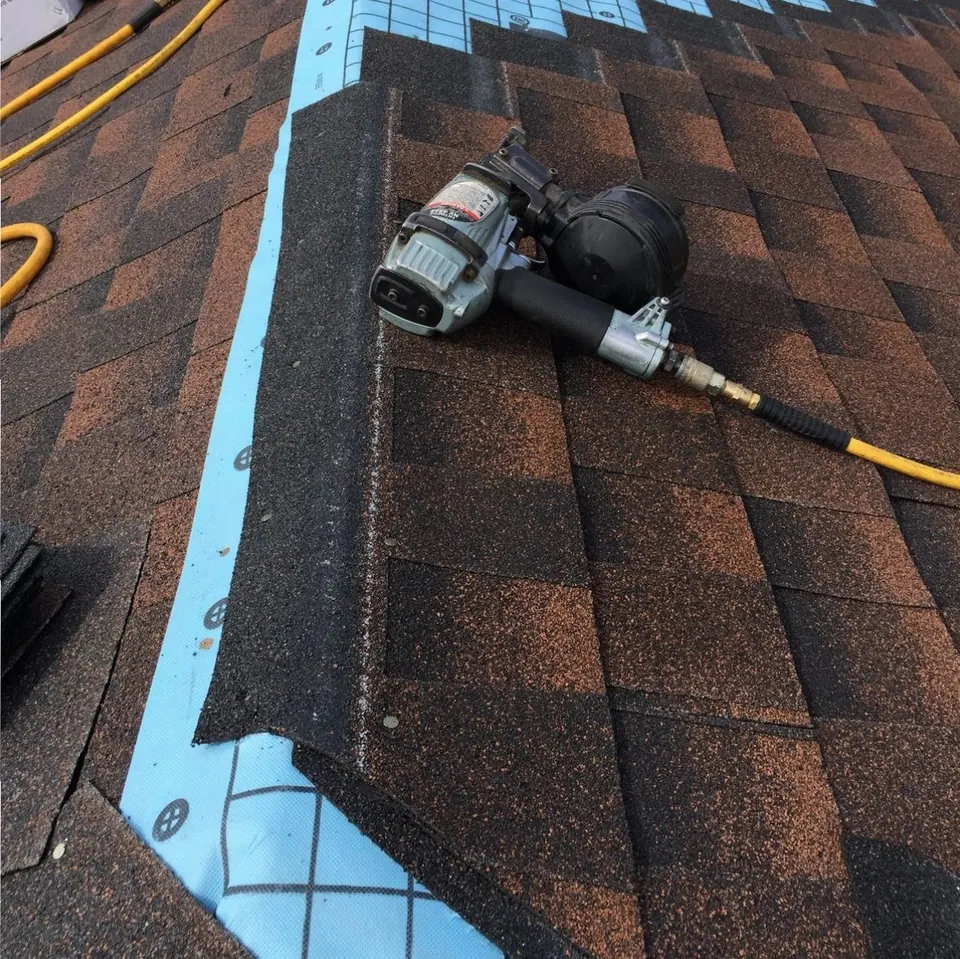 Ridge cap shingles going on over a blue ice and water membrane, with a roofing nailer