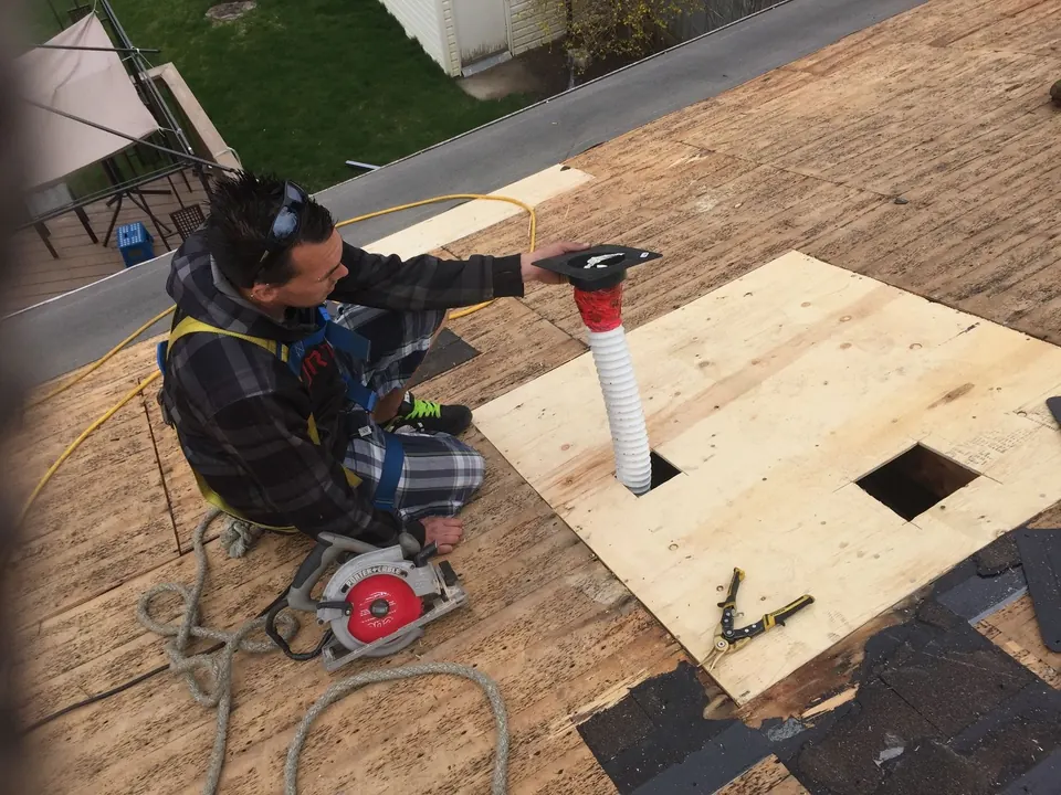A roofer fitting a vent through new plywood decking after the tear-off